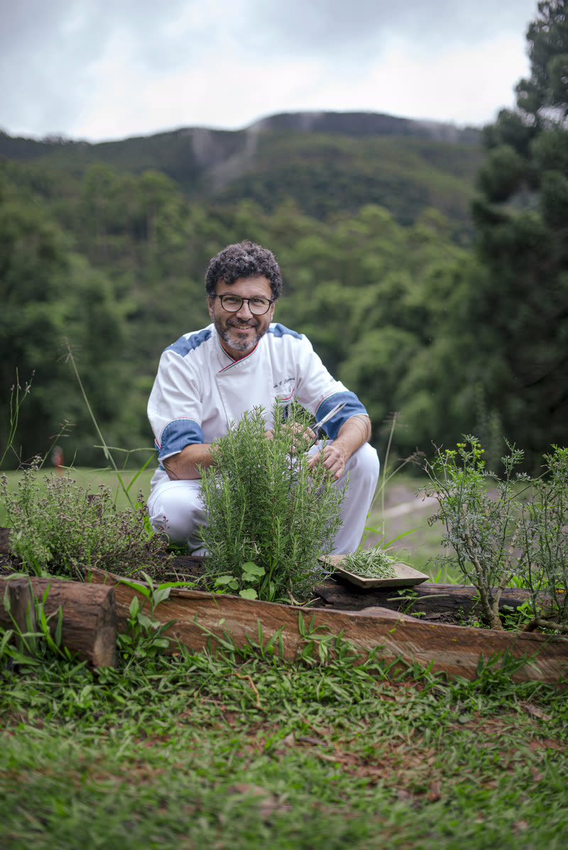 Gerardo agachado no canteiro de ervas, com o vale do Bom Jardim ao fundo.