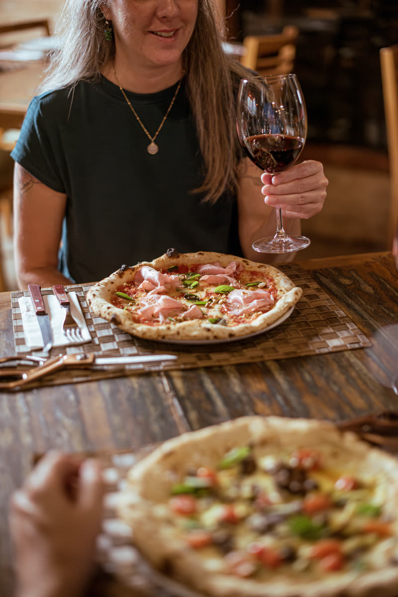 Mesa servida com duas pizzas napoletanas e taças de vinho tinto.